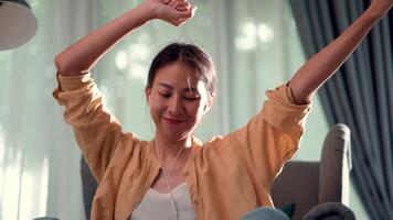 Young woman sitting on sofa in living room and use earphone for enjoy to dance while listening music from application on smartphone at home video