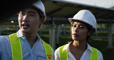 Slow motion shot, Asian Young Inspector Engineer man and female colleague wearing helmet standing and checking operation in solar farm, They are talking together