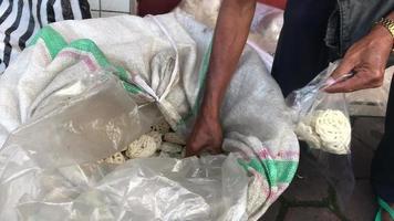 un hombre está envolviendo el pedido de galletas kerupuk de un cliente en una bolsa de plástico. video