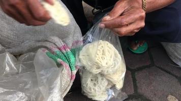 un hombre está envolviendo el pedido de galletas kerupuk de un cliente en una bolsa de plástico. video