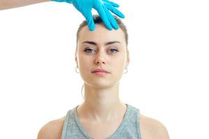 young girl without makeup stands up straight and the doctor in a blue glove touches her face close-up photo