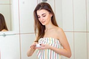 young beautiful girl stand towel in the bathroom and holding a cream photo