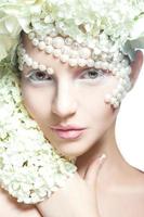 Beautiful young woman looking at camera in studio. Tender makeup and creative accessories with flowers photo