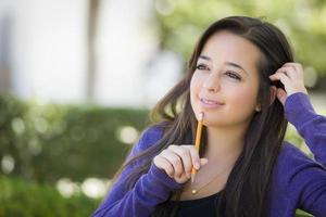 estudiante de raza mixta pensativa con lápiz en el campus foto