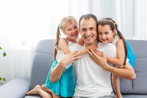 Happy dad carrying two little cute child girl on back giving kid piggyback ride having fun together, smiling single father playing with daughter embracing daddy laughing looking at camera, portrait photo