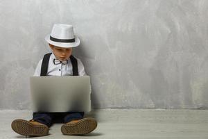 Little boy using laptop against grey wall background photo