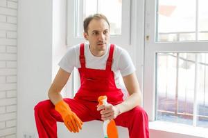 Male janitor cleaning a window in an office wearing an apron and gloves as he works photo