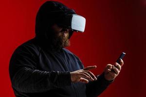 Virtual driving lessons concept. Hipster on excited face on high speed in virtual reality with modern digital gadget. Man with beard in VR glasses, red background. photo