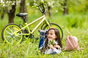 little girl with bike near flowering trees in spring photo