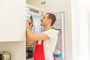 Repairman makes refrigerator appliance troubleshooting and maintenance works photo