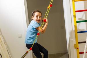 Portrait of a happy child in a gaming entertainment center. The sweating little girl hanging on a soft horizontal bar. A beautiful active baby goes in for sports. photo