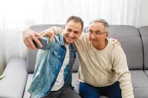 padre sonriente e hijo adulto fotografiando juntos en casa foto