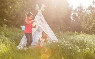 Two happy laughing little girls in camping tent in dandelion field photo