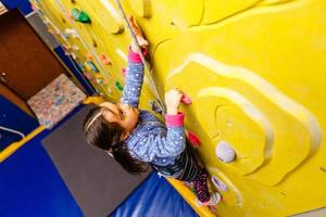 Little girl climbing a rock wall indoor photo