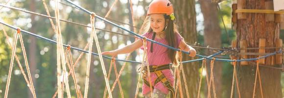 Adorable little girl enjoying her time in climbing adventure park on warm and sunny summer day. Summer activities for young kids. Child having fun on school vacations. photo