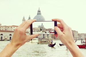tomando fotografías en un teléfono inteligente móvil en góndola en el canal grande con una casa antigua clásica en el fondo, venecia, italia foto