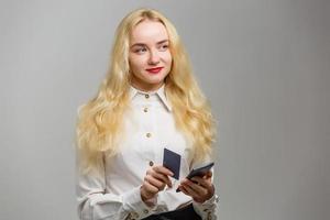 Portrait of a happy young blonde girl showing plastic credit card while holding mobile phone isolated over background photo