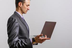 Working with joy. Handsome young man using his laptop and looking at camera with smile while standing against white background photo