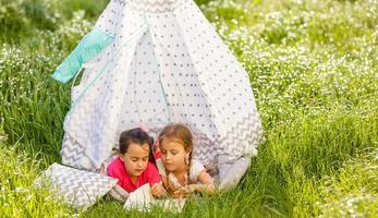 dos niñas riendo felices en una tienda de campaña en un campo de diente de león foto