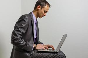 Positive young man using laptop computer over grey studio background photo