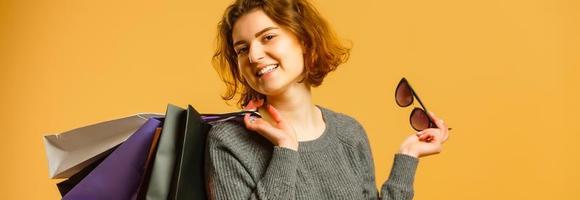 foto de una alegre y bonita mujer joven que se encuentra aislada sobre un fondo amarillo de pared. mirando a un lado sosteniendo bolsas de compras.