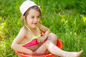 la niña se sienta en un lavabo con agua. día caluroso de verano foto