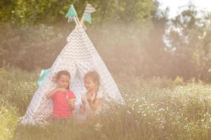 Two happy laughing little girls in camping tent in dandelion field photo