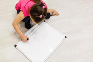 Image of young cute little child. Baby girl in class. Child stands near school chalk blackboard. Looking at camera. School concept. photo