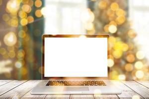 Image of open laptop with white screen on wooden table in front of christmas tree background. For mockup photo