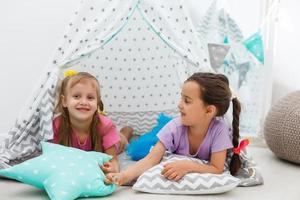Two cute happy girls play at home. Funny lovely sisters are having fun in children room. Girls play photo