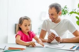 Handsome father and his cute little daughter are playing with paper planes and smiling while spending time together photo