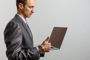 Positive young man using laptop computer over grey studio background photo