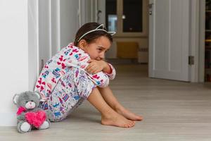 Sad little girl sitting near the wall photo