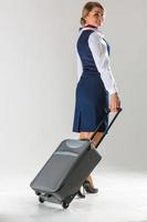 The stewardess goes and rolls her suitcase. White background. photo