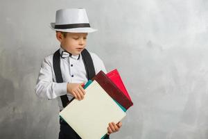 Back to school. Funny little boy in glasses pointing up on blackboard. Child from elementary school with book and bag. Education. Kid with a book photo