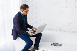 Doubtful young man looking up while working on laptop at home photo