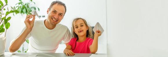 Handsome father and his cute little daughter are playing with paper planes and smiling while spending time together photo