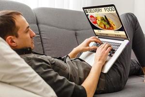 man lying on sofa and holding phone with app delivery food screen photo