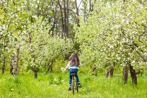 Child riding a bike on street with blooming cherry trees in the suburbs. Kid biking outdoors in urban park. Little girl on bicycle. Healthy preschool children summer activity. Kids play outside photo