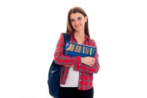 alegre y elegante estudiante inteligente con mochila en los hombros y carpetas para cuadernos en las manos posando y sonriendo en cámara aislada de fondo blanco foto