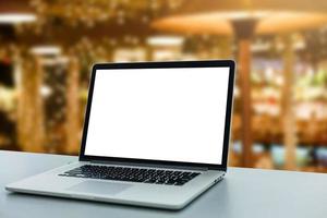 Image of open laptop with white screen on wooden table in front of christmas tree background. For mockup photo