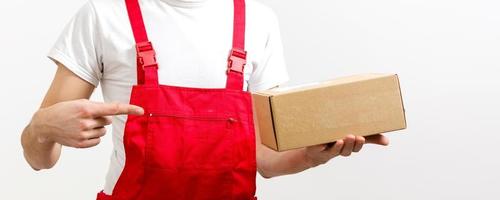 joven repartidor logístico sonriente con uniforme rojo sosteniendo la caja con fondo blanco foto