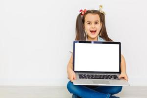 Cute little girl is sitting on floor with her laptop, wearing glasses, isolated over white photo