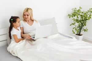 Young mother with toddler child working on the computer from home in bed photo