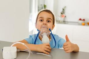 Little girl in a mask for inhalations, making inhalation with nebulizer at home inhaler on the table, indoor, sick child photo