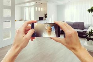 dos manos sosteniendo un teléfono inteligente móvil y tomando una foto en una moderna sala de estar y cocina de lujo