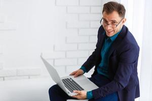 Handsome young man wearing glasses and working with touchpad while sitting on the couch in office photo