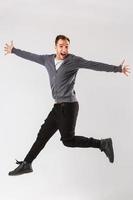 Photo of cheerful young man dressed in black t-shirt jumping over white background looking at camera.