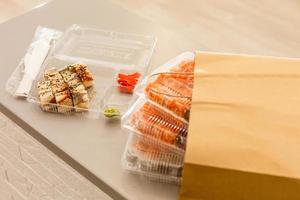 Sushi rolls in plastic box near paper package on white table. Delivery. Take away. photo