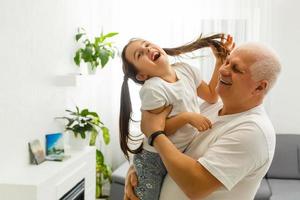 hombre caucásico de mediana edad jugando con una niña en la orilla del río. el hombre se para y sostiene a su nieta sobre su espalda mientras ella vuela, todos felices foto